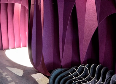 A purple wall featuring acoustic panels, a chair, and a window, creating a cozy and sound-friendly space.